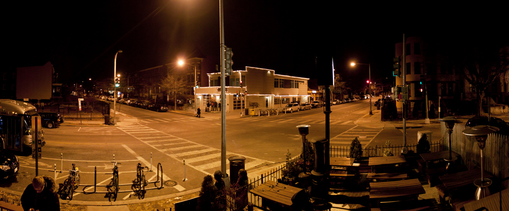 Nighttime street intersection with illuminated buildings and warm amber streetlights, calm and inviting neighborhood atmosphere.